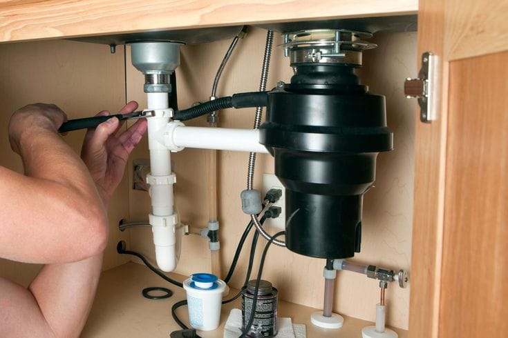 Plumber installing a garbage disposal beneath a kitchen sink in Danville